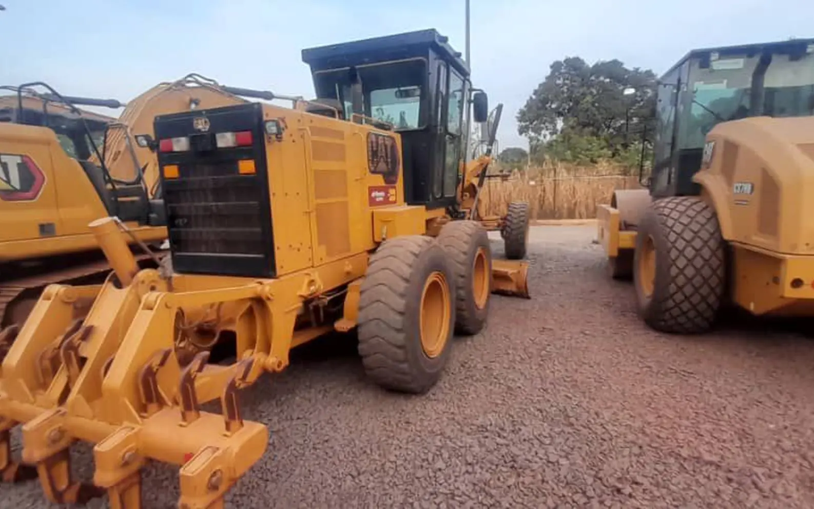 Niveleuse, compacteur et pelle hydraulique Caterpillar stationnés sur une piste en latérite d'un chantier de travaux publics